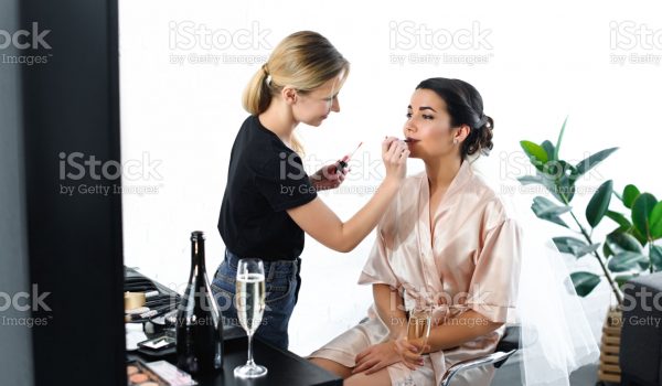 side view of makeup artist applying lipstick on brides lips
