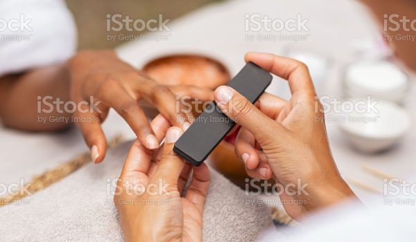 Close up of african hands of a qualified manicurist filing the nails of a young woman. Hands during manicure care session. Detail of a girl in a nail salon receiving manicure.