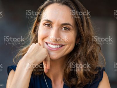 Portrait of a happy smiling mature woman with hand on chin looking at camera. Close up face of beautiful latin woman with brown hair outdoor. Cheerful hispanic woman closeup.